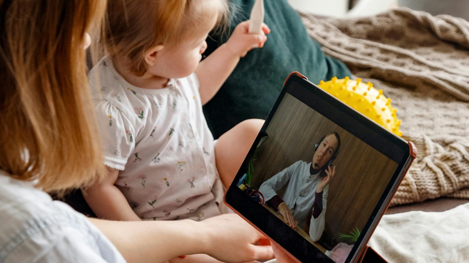 Woman using telehealth on her tablet next to baby